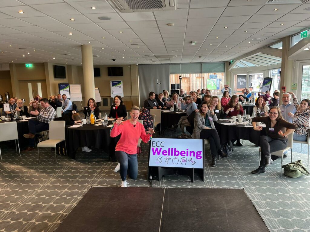 Leanne on one knee doing tiger pose whilst delivering a wellbeing keynote sharing the cadence approach to a room full of people