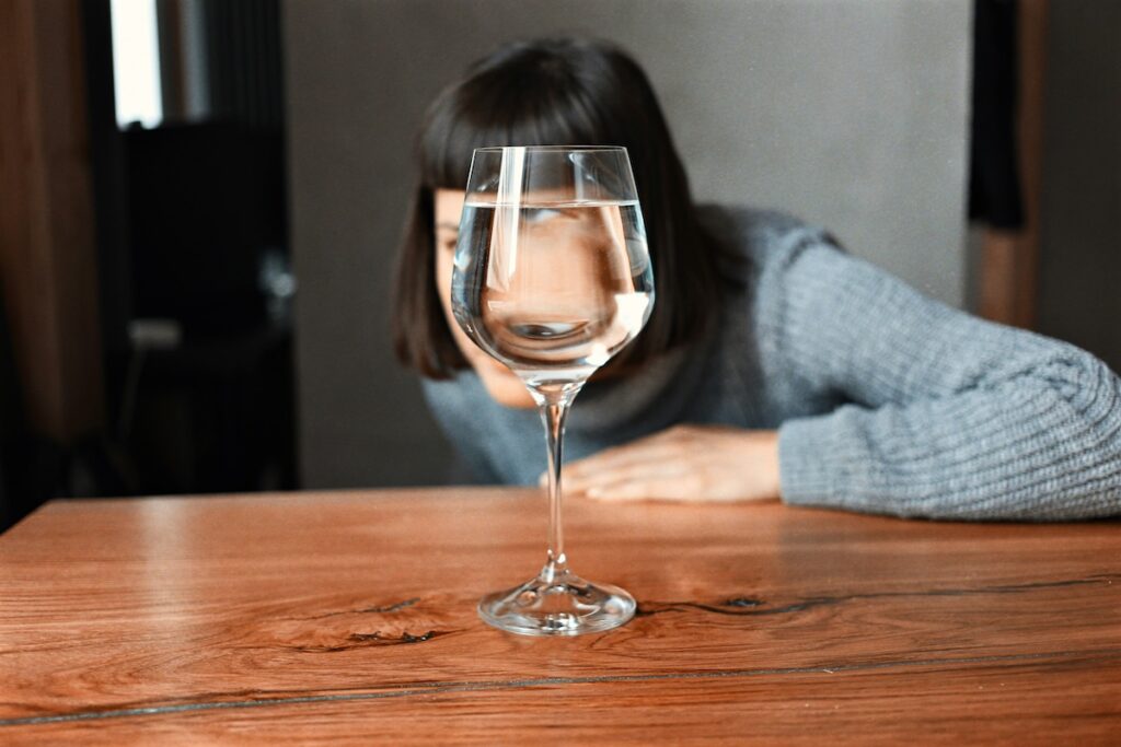 Why I Stopped Drinking—and a Reflection for the Sober Curious - wopman looking through a wine glass of water with her eye distorted