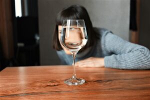 Why I Stopped Drinking—and a Reflection for the Sober Curious - wopman looking through a wine glass of water with her eye distorted